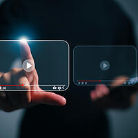 Eine Person die auf ein Bildschirmsymbol tippt, auf dem ein Video abspielen Symbol gezeigt wird. 