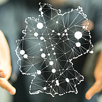 Zwei Hände, die eine stilisierte Landkarte von Deutschland umschließen, auf der digitale Netze dargestellt sind.