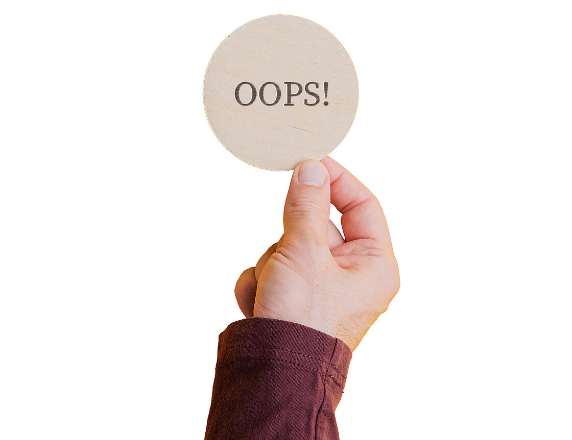 Hand, die ein Schild mit dem Wort "Oops" hochhält