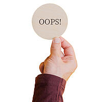 Hand, die ein Schild mit dem Wort "Oops" hochhält